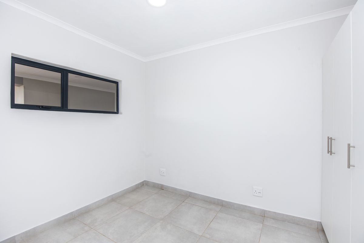 A clean, neutral bedroom featuring tiled flooring, built-in cupboards, and a high-level window, providing a bright and versatile living space.