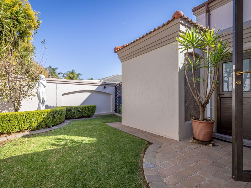 A well-maintained rear garden area featuring a paved patio, manicured hedges, and a secure boundary wall.
