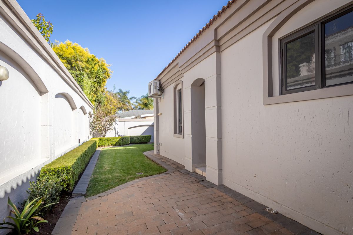A well-maintained rear exterior area featuring a paved walkway, manicured lawn, and neat hedging along the boundary wall.