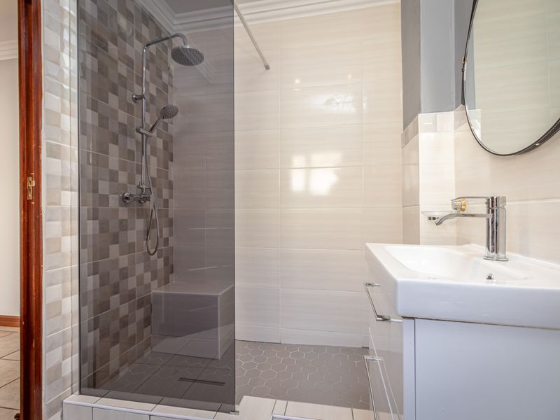 Modern bathroom featuring a spacious walk-in shower with glass screen, contemporary vanity basin, and stylish neutral wall and floor tiling.