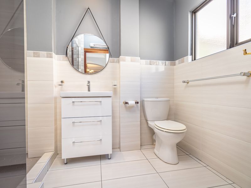 A modern, well-maintained bathroom featuring a vanity basin, toilet, and a glass-enclosed shower with neutral wall and floor tiling.