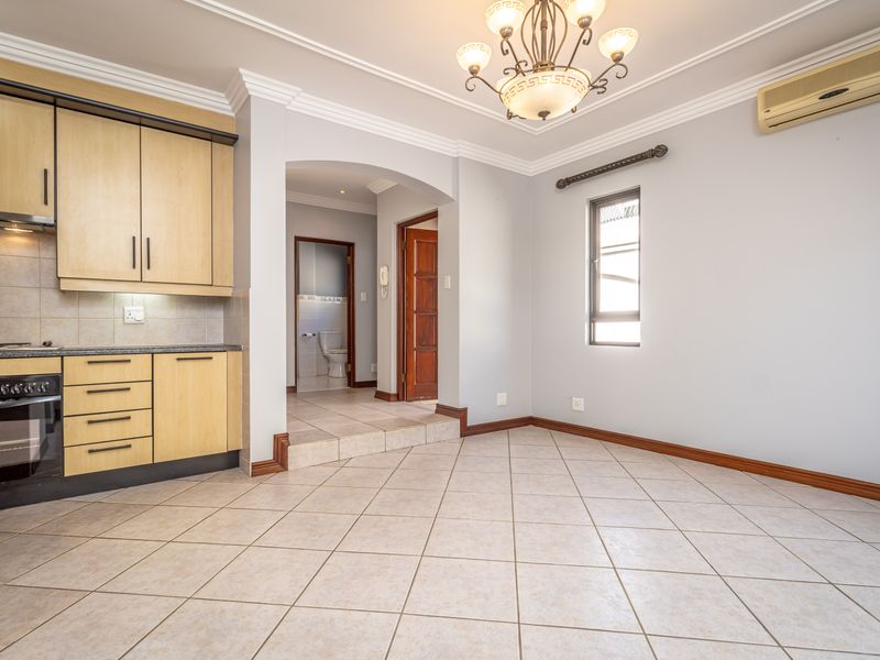 An open-plan kitchen and living area featuring tiled floors, built-in cabinetry with integrated appliances, and an archway leading to a bathroom.