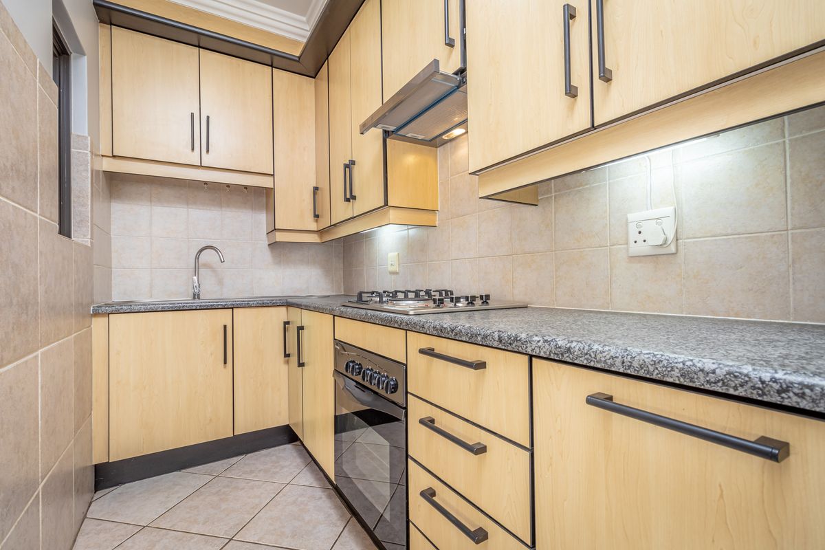 A functional kitchen featuring light wood cabinetry, granite countertops, a gas hob, built-in oven, and tiled finishes throughout.