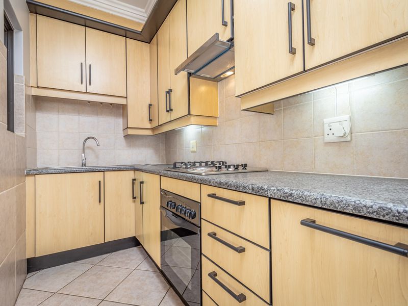 A functional kitchen featuring light wood cabinetry, granite countertops, a gas hob, built-in oven, and tiled finishes throughout.
