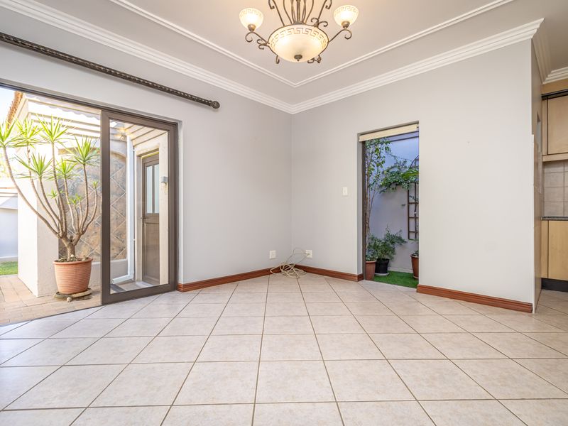 An open-plan living area featuring tiled floors, crown molding, and direct access to an outdoor courtyard, adjacent to a compact kitchen space.