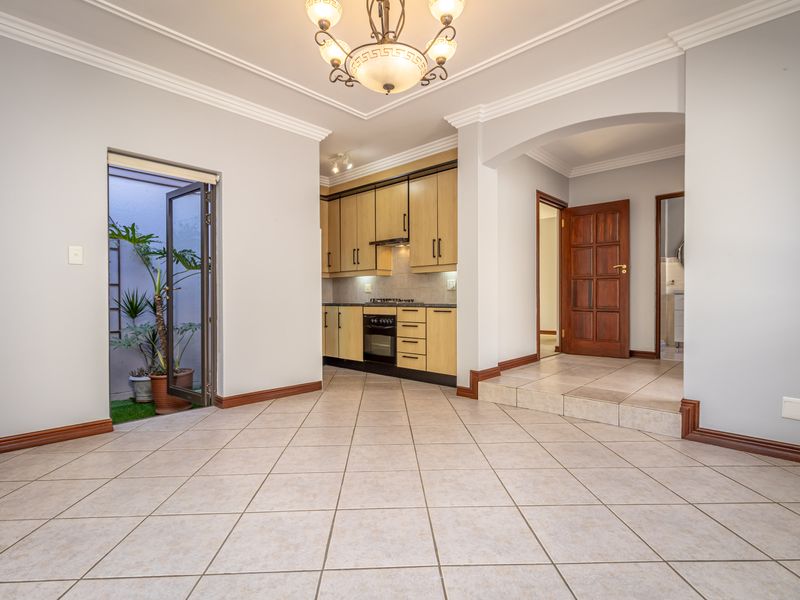 Open plan living area featuring tiled floors, coved cornicing, and a compact kitchen with built-in cabinetry, gas hob, and oven, leading to an outdoor space.