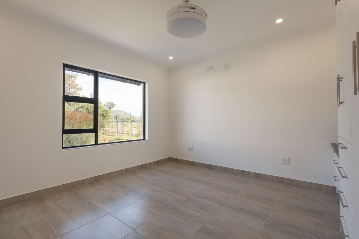 A bright, empty bedroom featuring neutral tiled flooring, modern black-framed windows, and built-in cabinetry.
