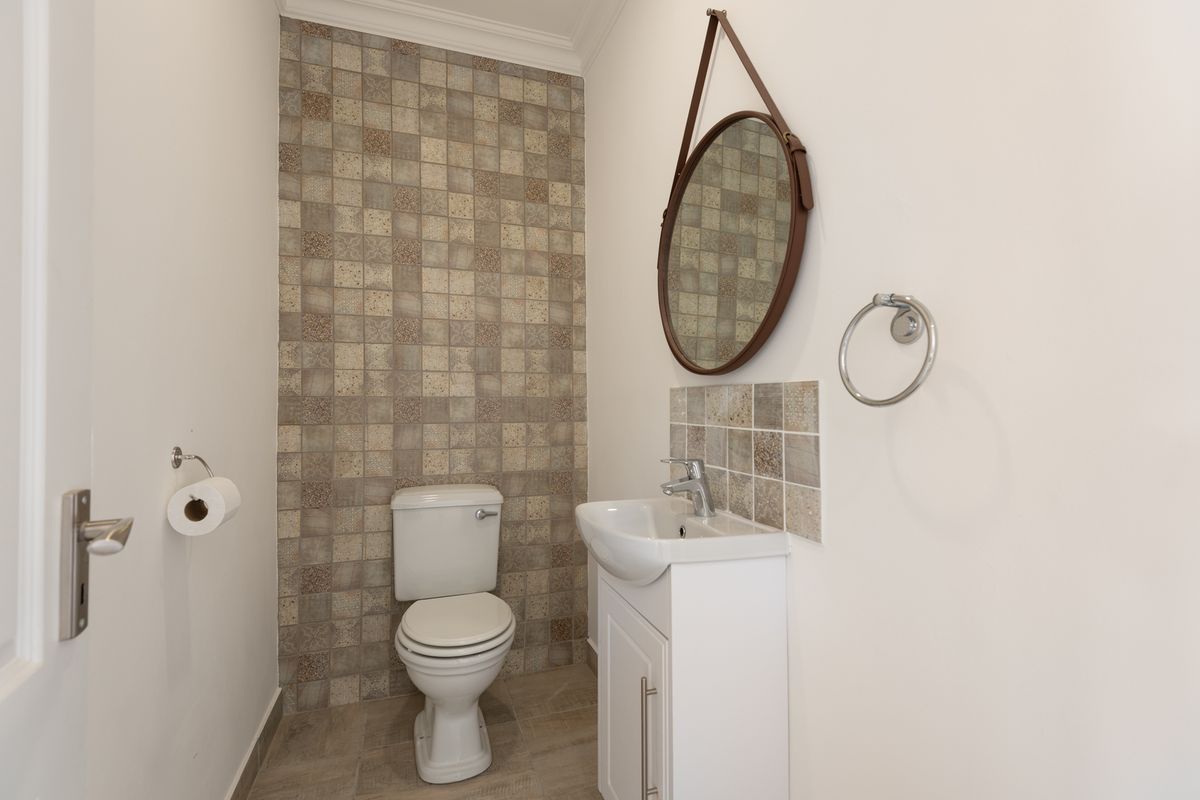 A compact guest bathroom featuring a modern vanity, wall-mounted basin, and decorative tiled feature wall.