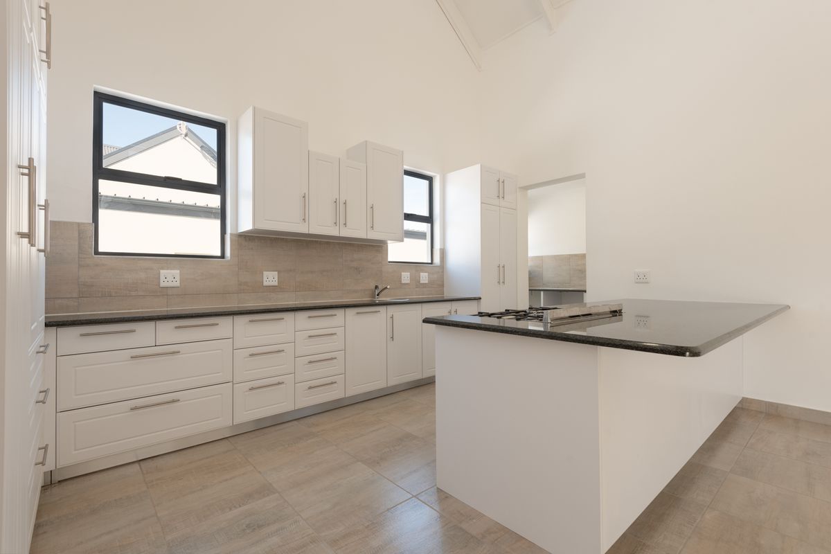 Modern kitchen featuring white cabinetry, granite countertops, a central island with a built-in gas hob, and tiled flooring under a vaulted ceiling.