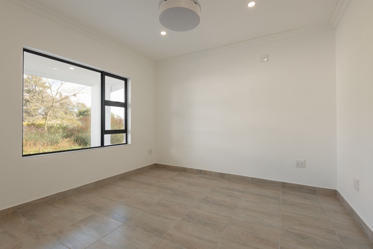 A bright, empty bedroom featuring neutral tiled flooring, clean white walls, and a large window providing natural light and garden views.