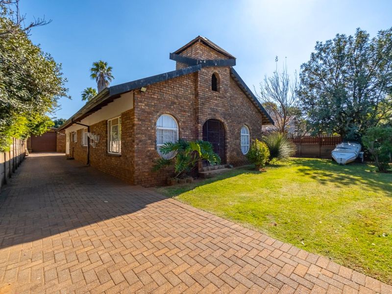 A charming face-brick house featuring a paved driveway, arched windows, and a well-maintained front garden area.