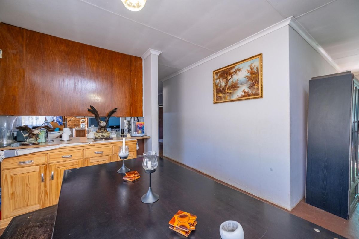A dated kitchen area featuring wooden cabinetry, a mirror splashback, and laminate countertops, offering potential for a modern renovation.