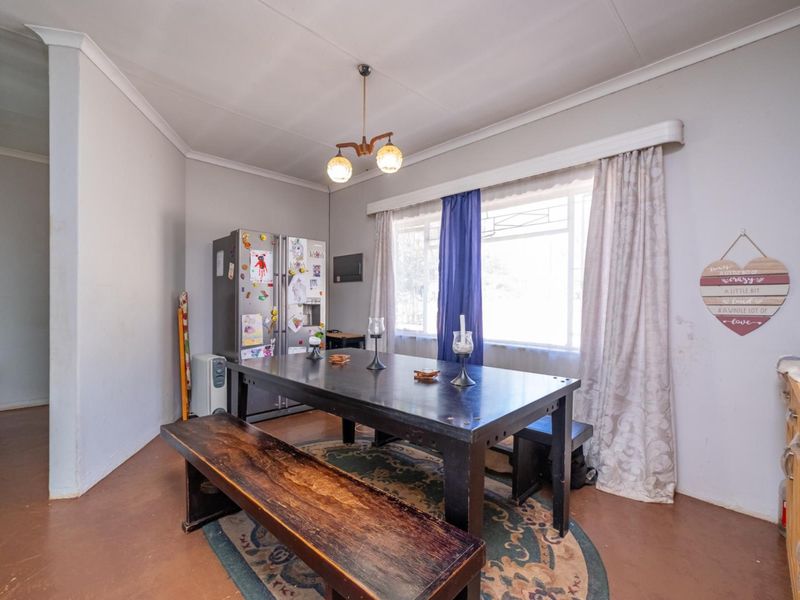 A dining room featuring a large window, pendant lighting, and ceiling cornices, requiring cosmetic updates to the walls and flooring.