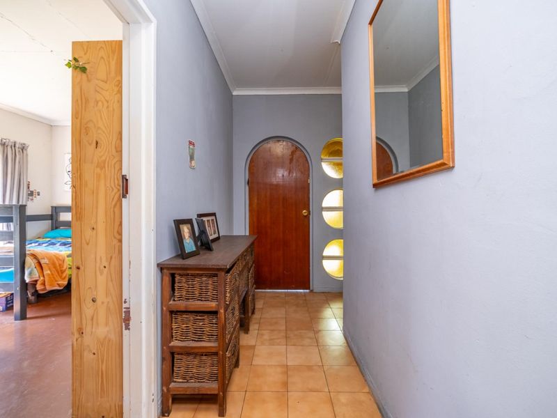 A functional hallway featuring tiled flooring, an arched wooden entrance door with circular glass accents, and access to an adjacent bedroom.
