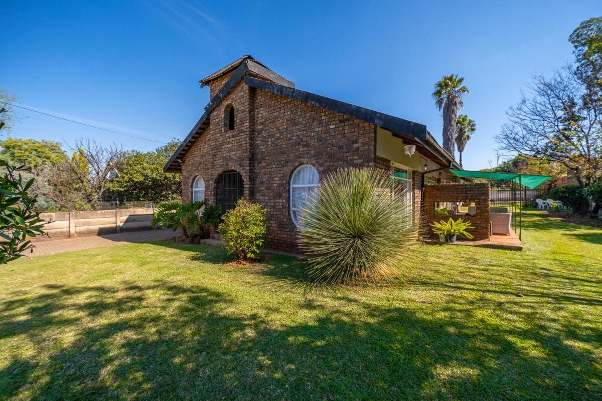 A view of the rear exterior featuring a face brick facade, arched windows, and a covered patio area overlooking a well-maintained garden.