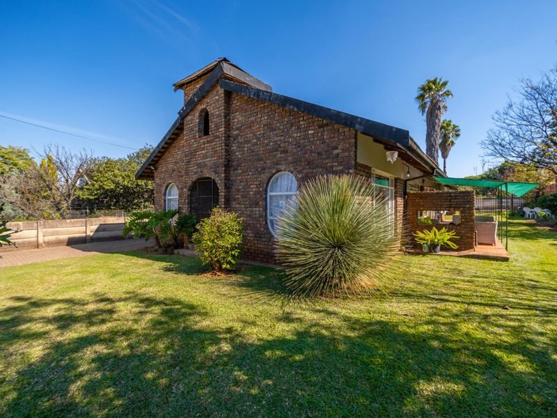 A view of the rear exterior featuring a face brick facade, arched windows, and a covered patio area overlooking a well-maintained garden.