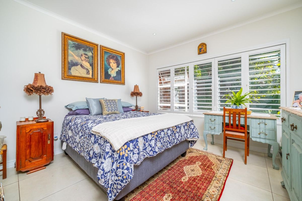 A well-lit bedroom featuring neutral tiled flooring, recessed downlights, and white plantation shutters providing natural light and privacy.