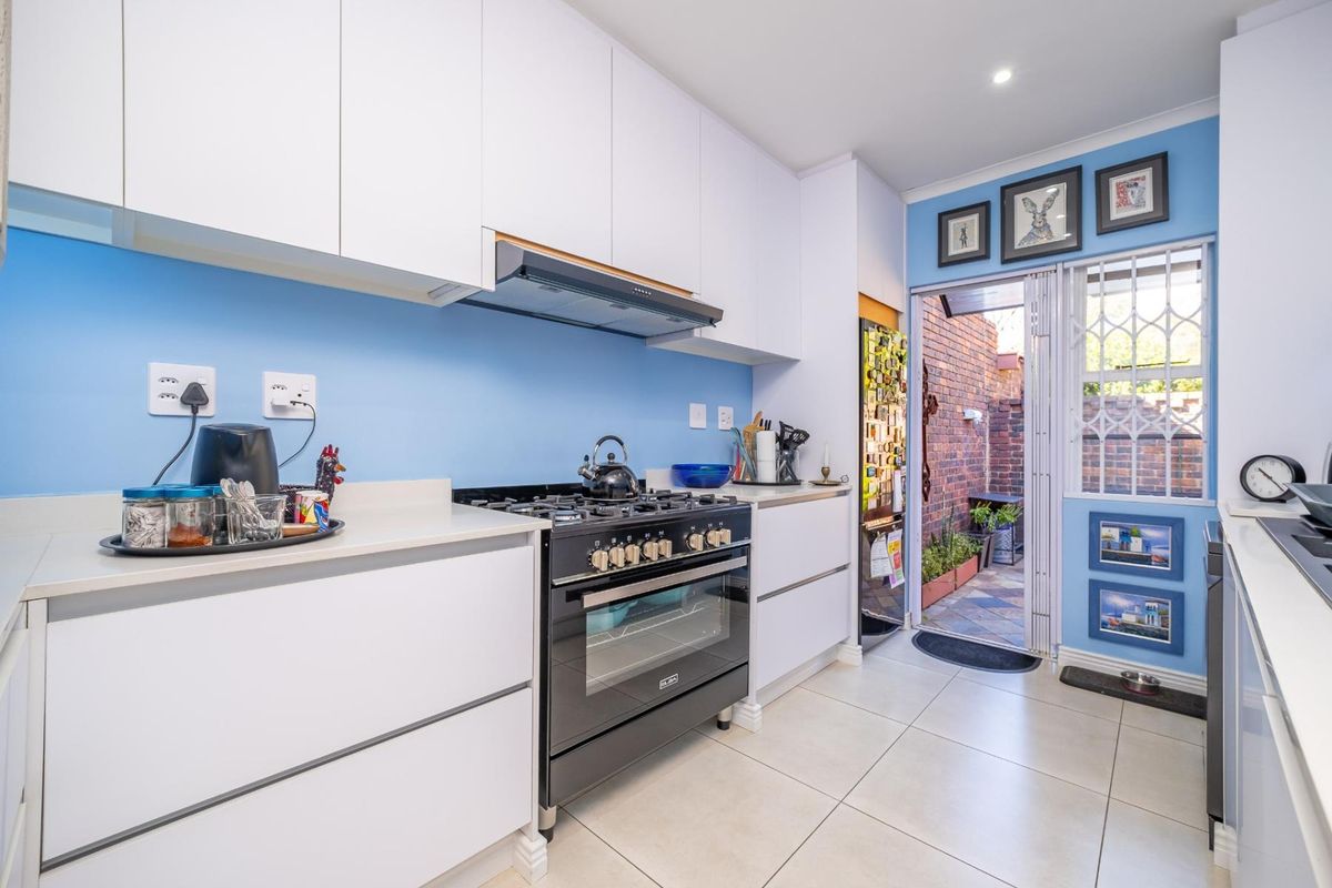 Modern kitchen featuring white cabinetry, stone countertops, a gas stove with oven, and direct access to a private rear courtyard.