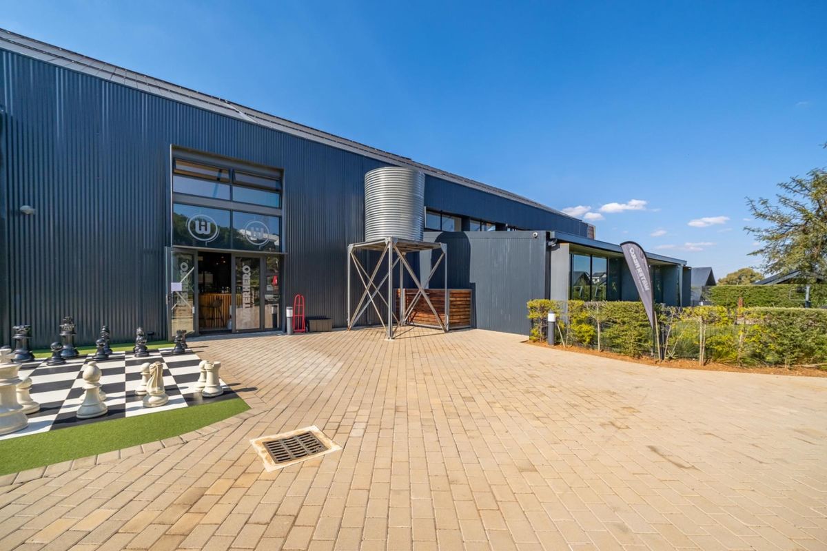 Exterior view of a modern industrial-style building featuring corrugated metal cladding, a paved courtyard, and an elevated water tank.