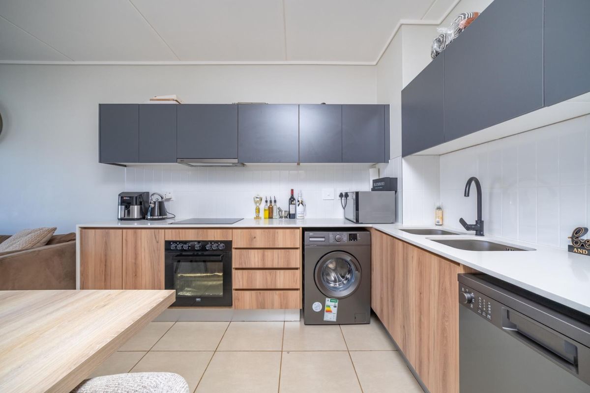 Modern kitchen featuring wood-grain lower cabinetry, dark grey upper cabinets, white countertops, integrated oven, hob, extractor fan, and built-in laundry appliance space.