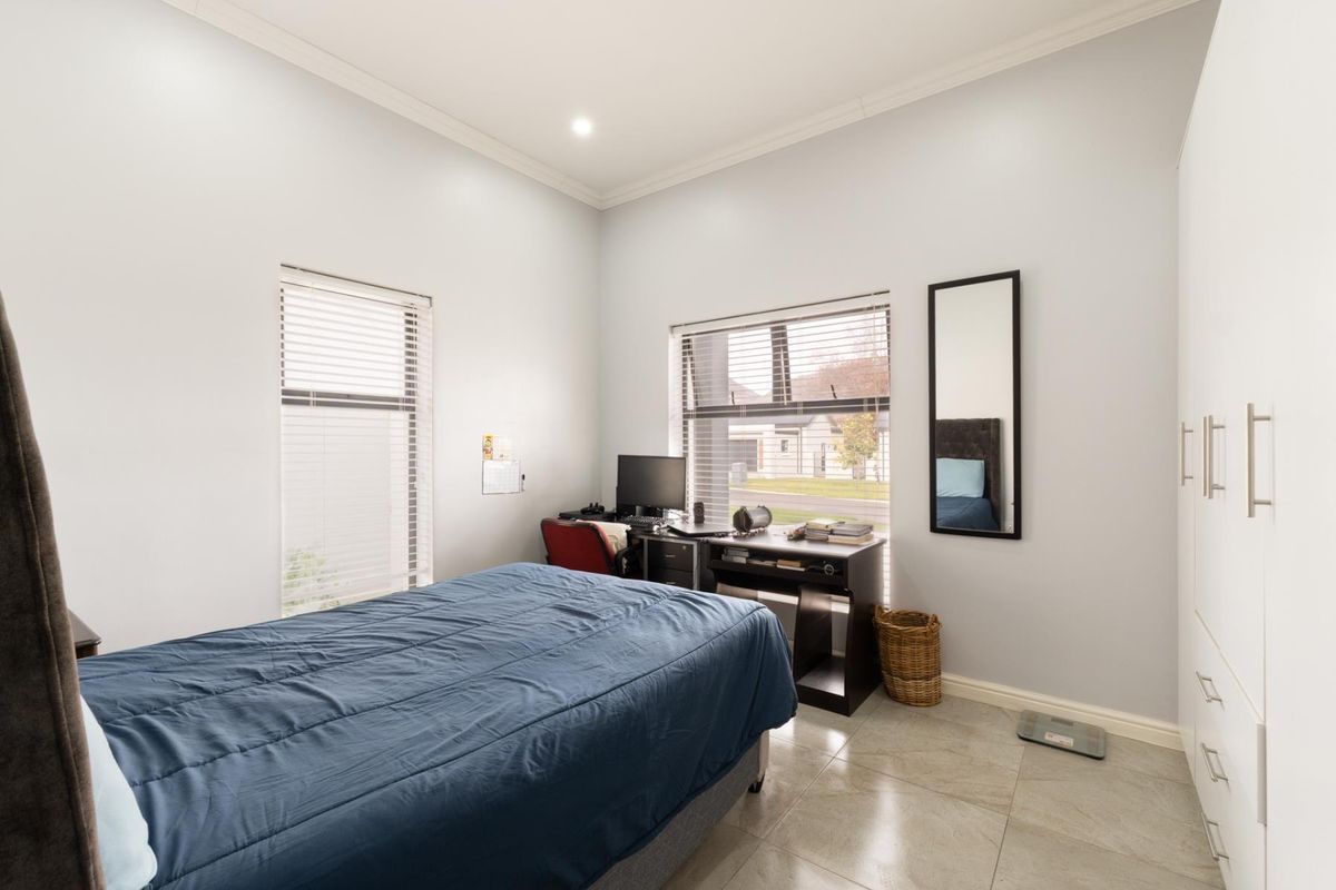 A bright bedroom featuring tiled flooring, built-in cupboards, and large windows with venetian blinds, offering a clean and functional living space.