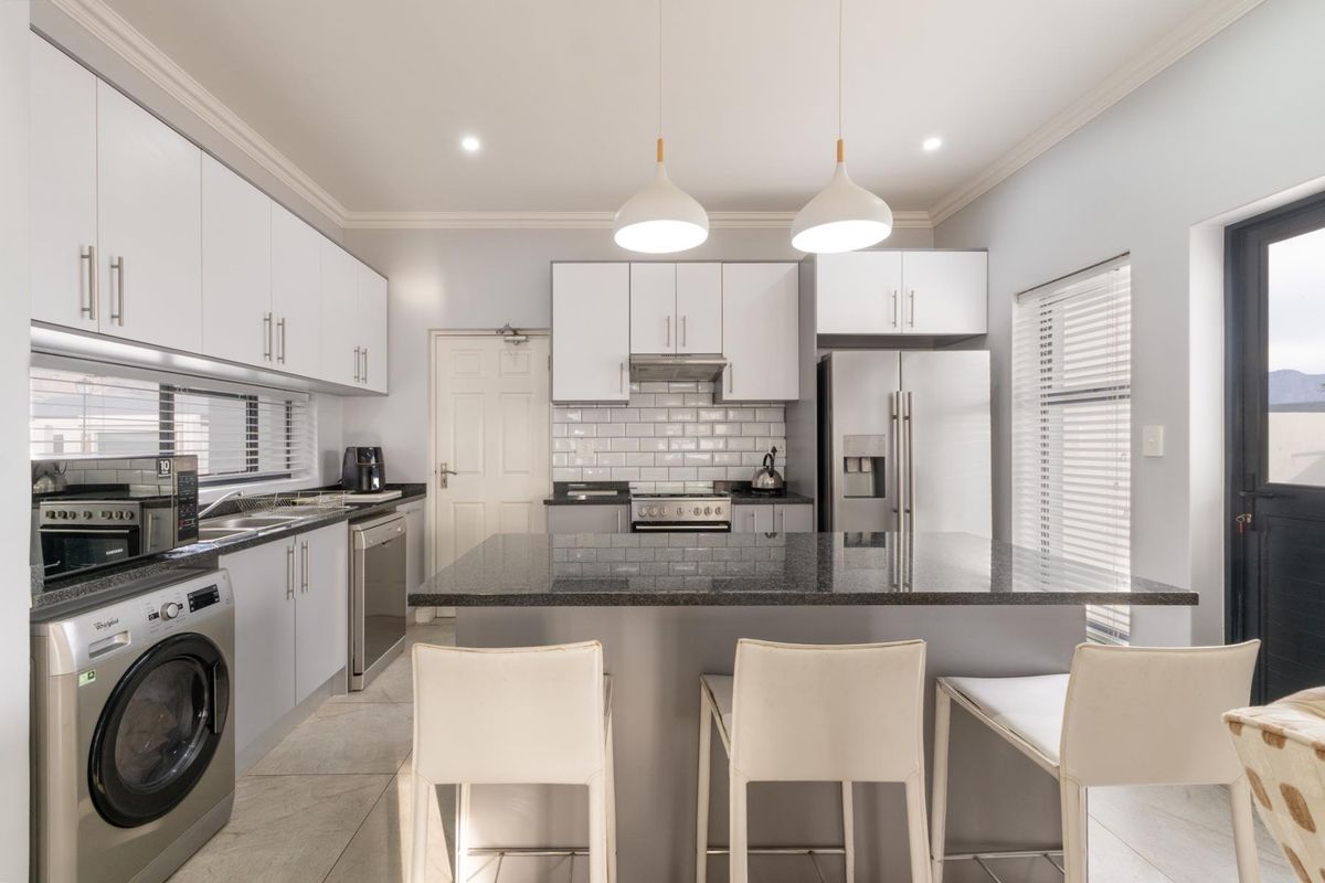 Modern kitchen featuring white cabinetry, granite countertops, a central island with breakfast bar, subway tile backsplash, and integrated stainless steel appliances.