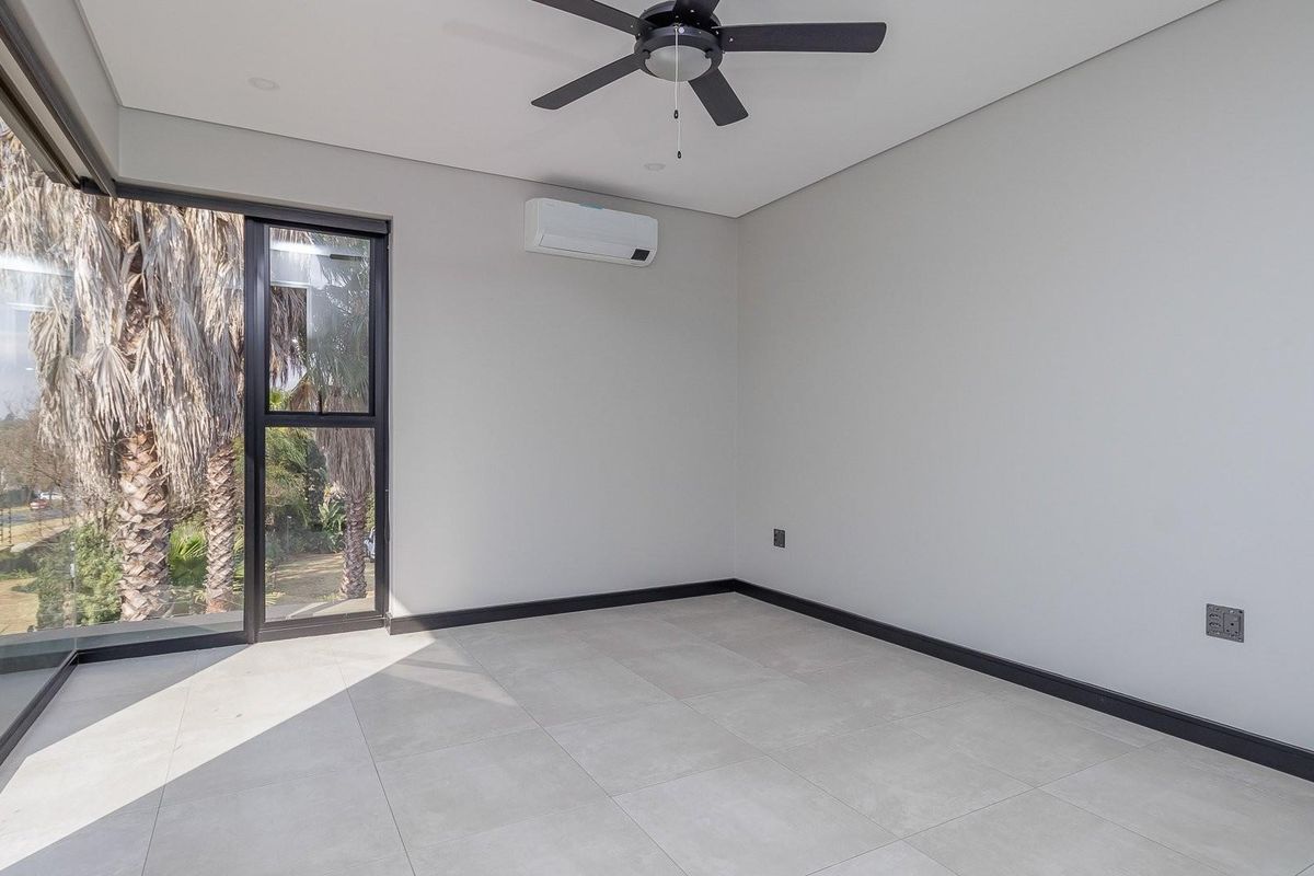 A bright, modern bedroom featuring large glass sliding doors, tiled flooring, a ceiling fan, and a wall-mounted air conditioning unit.