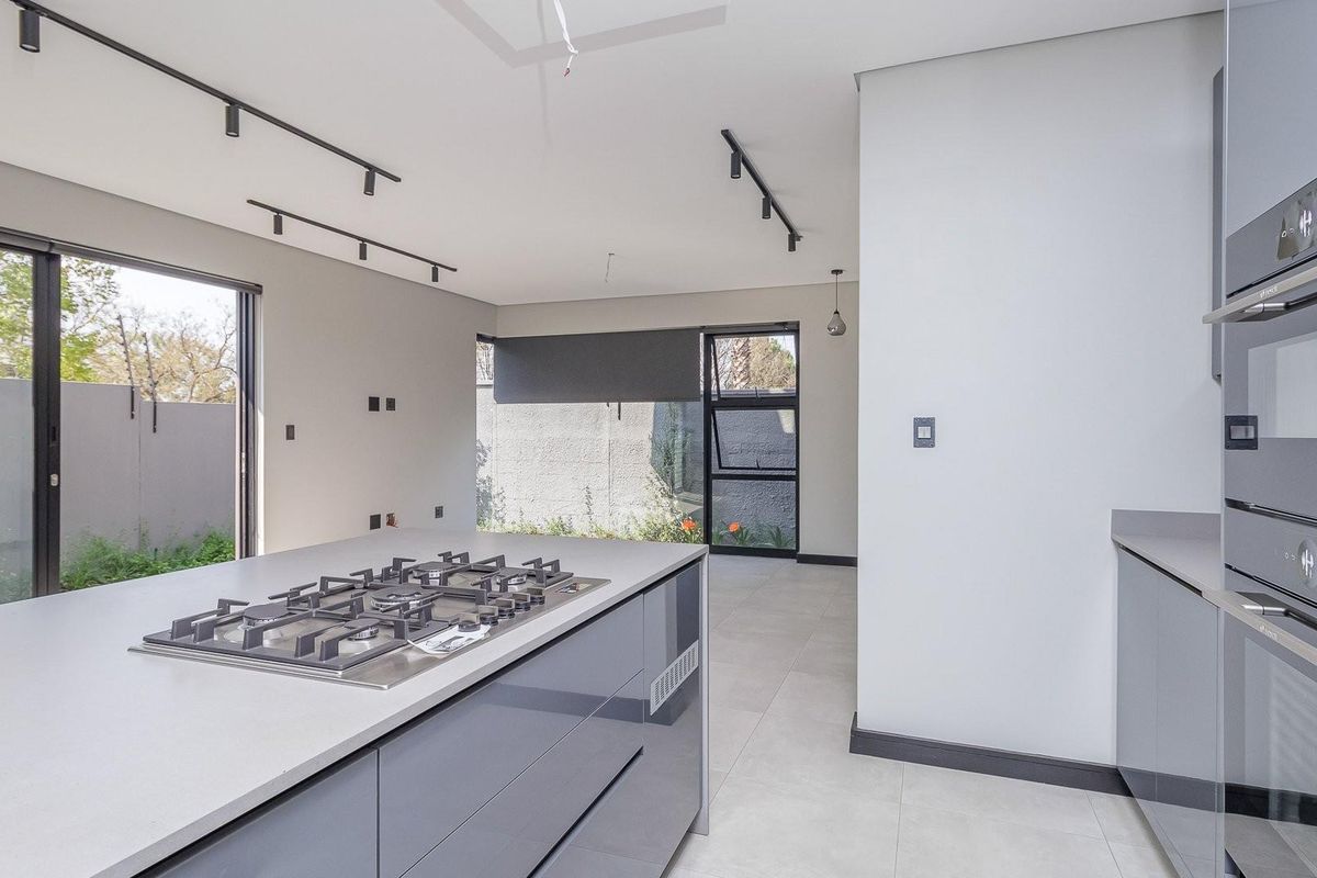 Modern open-plan kitchen featuring a central island with a built-in gas hob, sleek grey cabinetry, and integrated wall ovens, opening to a private garden.