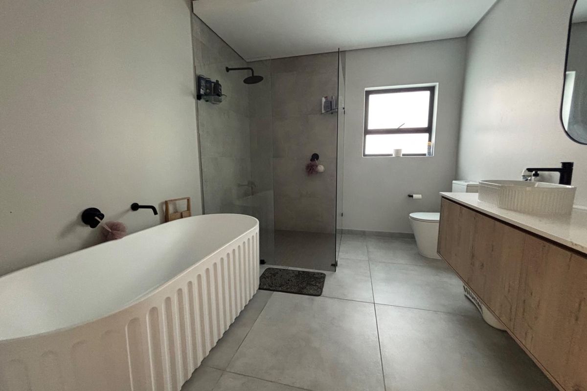 Modern bathroom featuring a freestanding fluted bathtub, walk-in glass shower, wall-mounted matte black fixtures, and a floating vanity with a vessel sink.