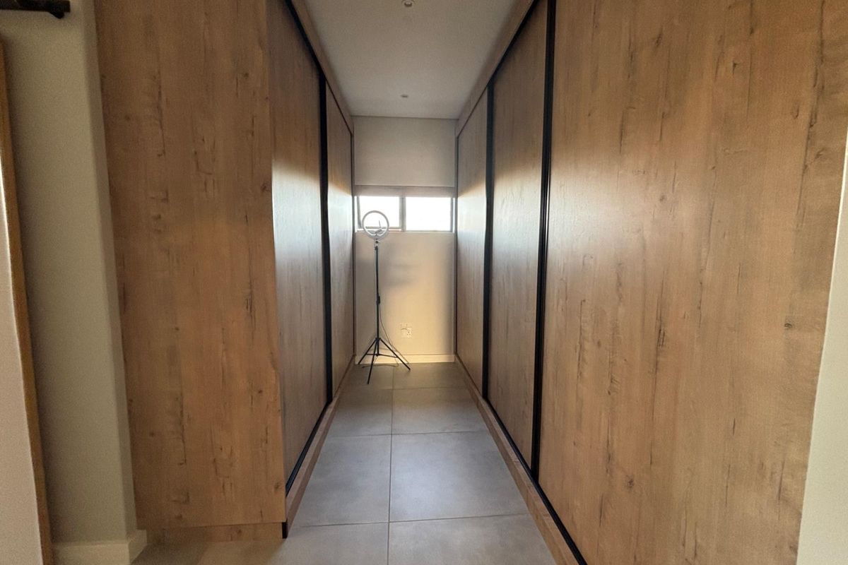 A modern walk-in closet or dressing area featuring floor-to-ceiling wood-grain built-in cabinetry with sliding doors and large format floor tiles.