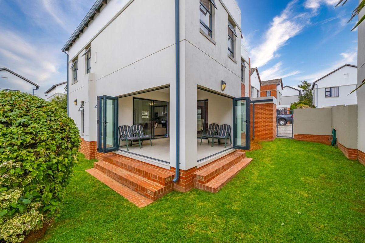 Rear view of the property featuring a covered patio with bi-fold doors, brick steps, and a well-maintained garden area.