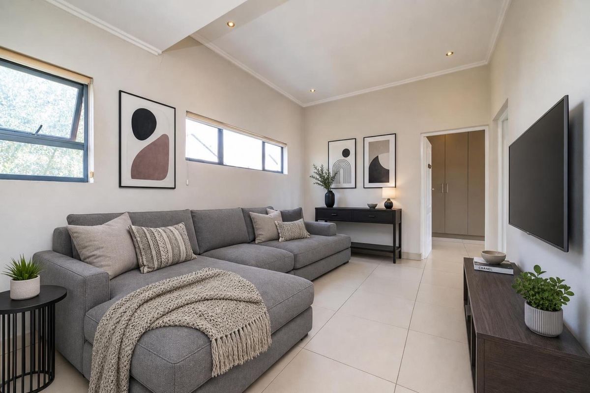 A well-maintained living room featuring neutral tiled flooring, recessed downlighting, and clean finishes, with an adjacent hallway leading to built-in storage.