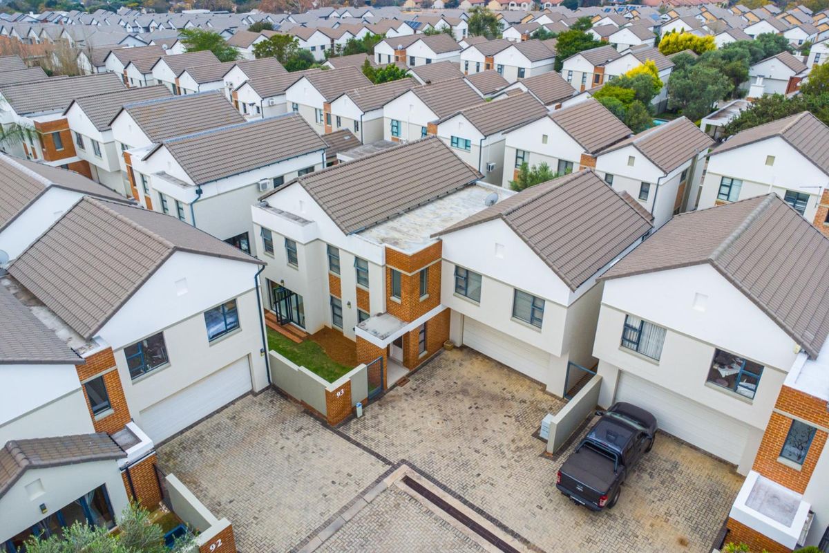 Aerial view of a residential estate featuring multiple modern townhouses with tiled roofs, paved driveways, and secure boundary walls.