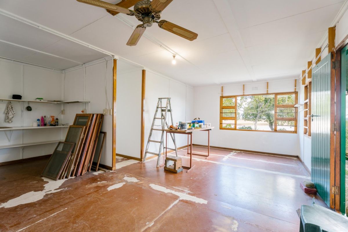 An interior room featuring exposed floor surfaces, a ceiling fan, and large windows, currently undergoing maintenance or renovation work.