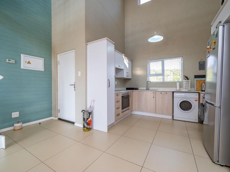 Open-plan kitchen area featuring modern cabinetry, built-in appliances, tiled flooring, and high ceilings, seamlessly integrated with the living space and staircase access.