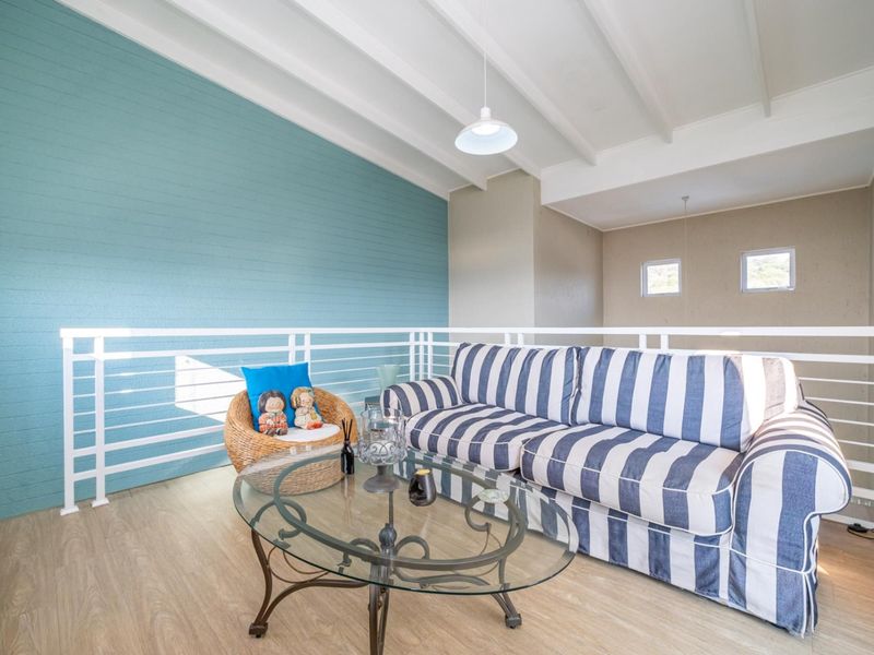 A bright living area featuring a vaulted ceiling with exposed beams, a modern metal balustrade, and light-toned laminate flooring.