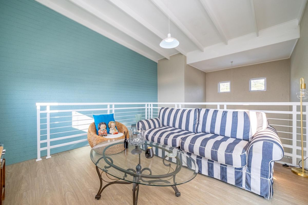 A bright living area featuring a vaulted ceiling with exposed beams, a modern metal balustrade, and light-toned laminate flooring.