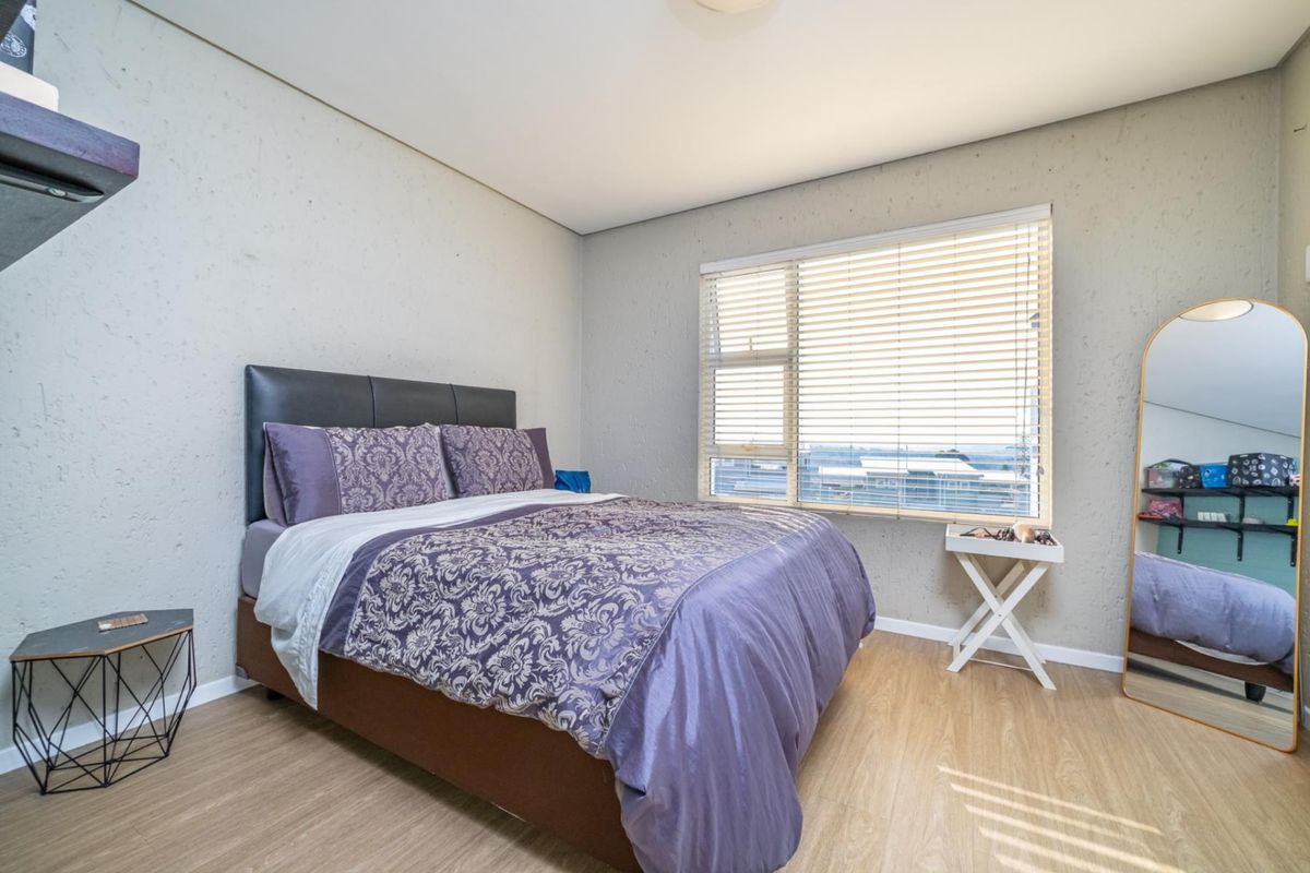 A well-lit bedroom featuring textured walls, laminate flooring, and a large window with fitted venetian blinds.