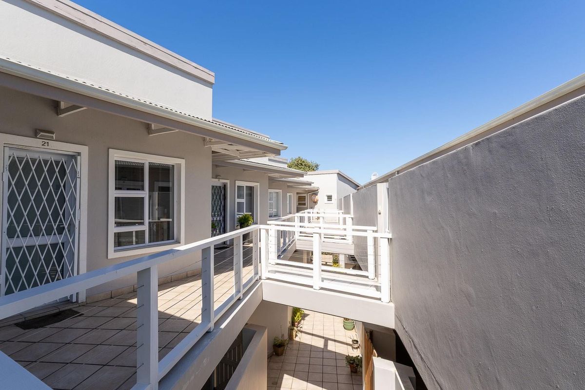 Exterior view of an apartment complex featuring a raised walkway, tiled balcony areas, and secure metal security gates on the unit entrances.