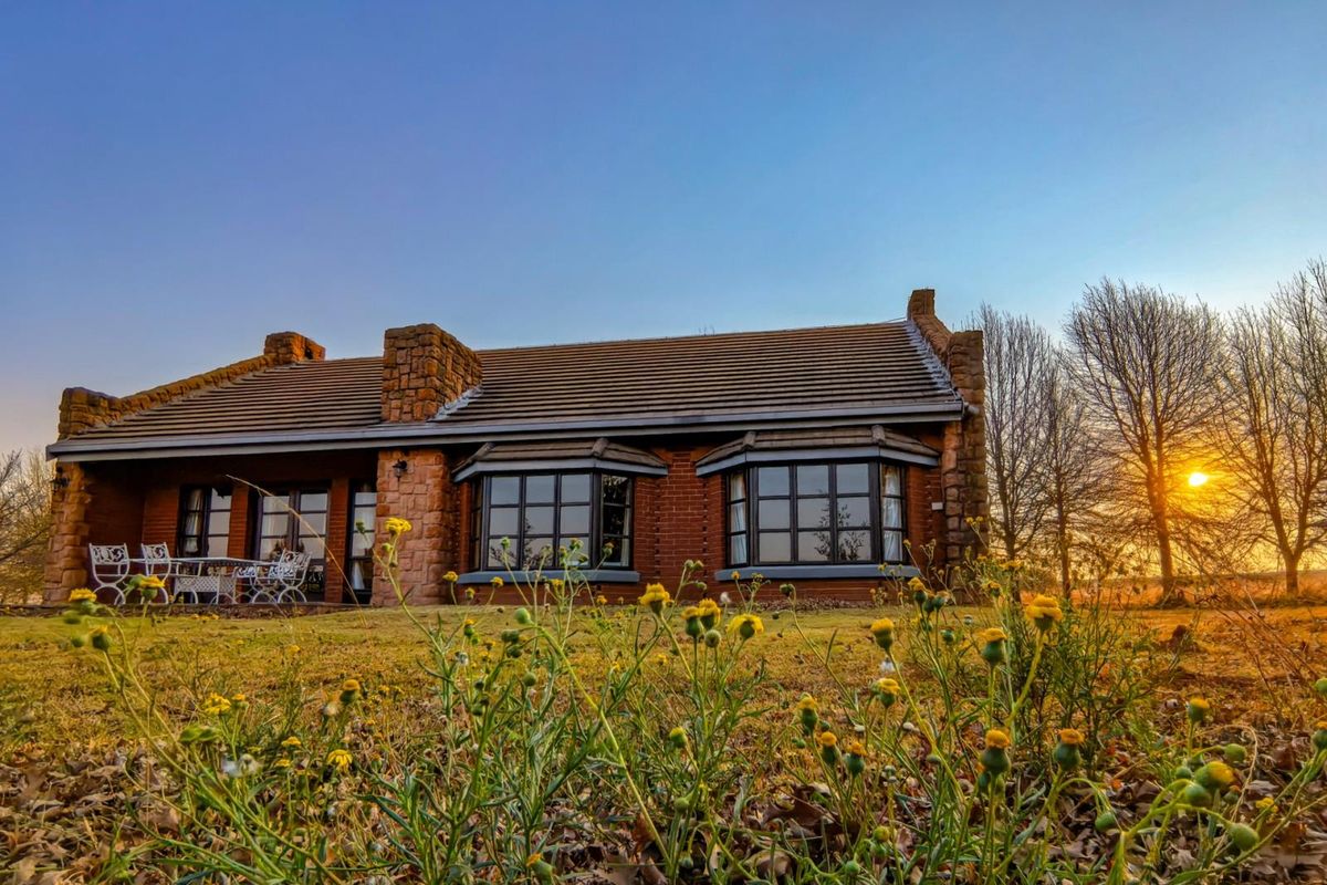 A charming brick house with stone accents and bay windows, featuring a covered patio area set against a scenic sunset backdrop.