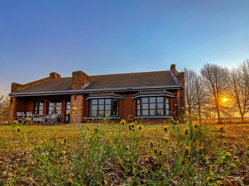 A charming brick house with stone accents and bay windows, featuring a covered patio area set against a scenic sunset backdrop.