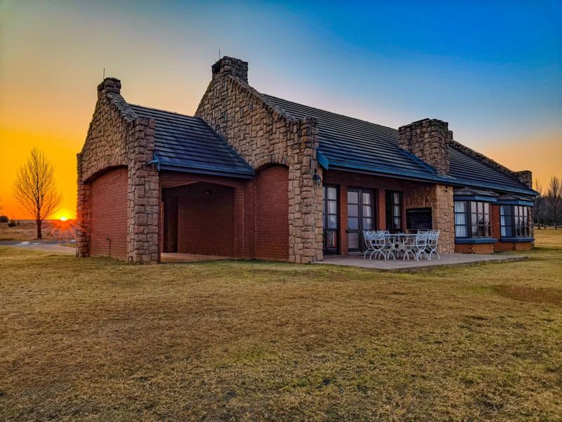 A charming stone and brick residence featuring a paved rear patio, bay windows, and a sunset view over the surrounding landscape.