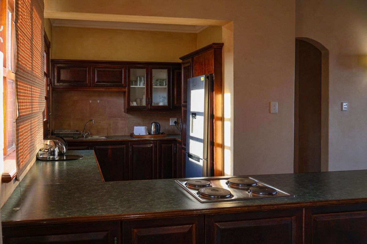 A functional kitchen featuring dark wood cabinetry, laminate countertops, a built-in electric hob, and a tiled backsplash with a stainless steel sink.