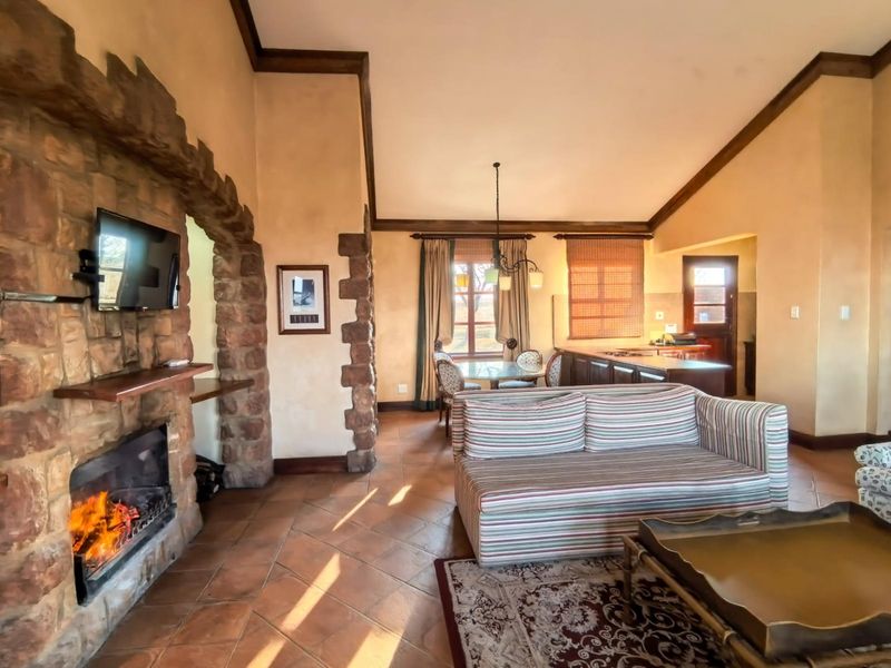 Open-plan living and dining area featuring a rustic stone fireplace, vaulted ceilings, and terracotta floor tiles, flowing into a functional kitchen space.