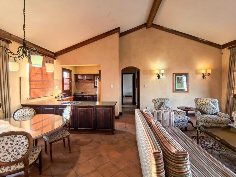 Spacious open-plan living and dining area featuring vaulted ceilings with exposed timber beams, terracotta flooring, and a functional kitchen with dark wood cabinetry.
