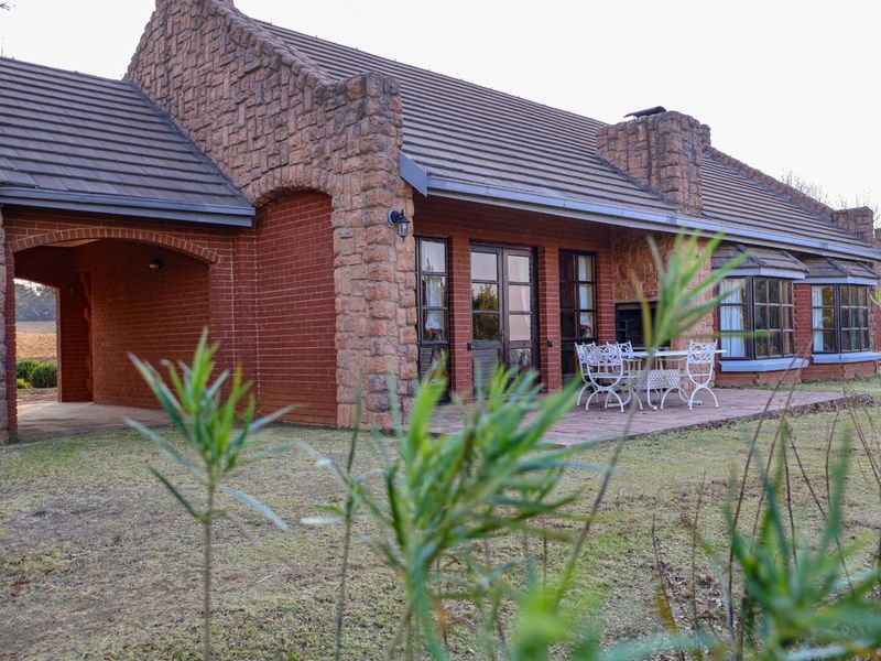 Rear view of a house featuring stone and brick masonry, a covered patio area, and bay windows overlooking the garden.