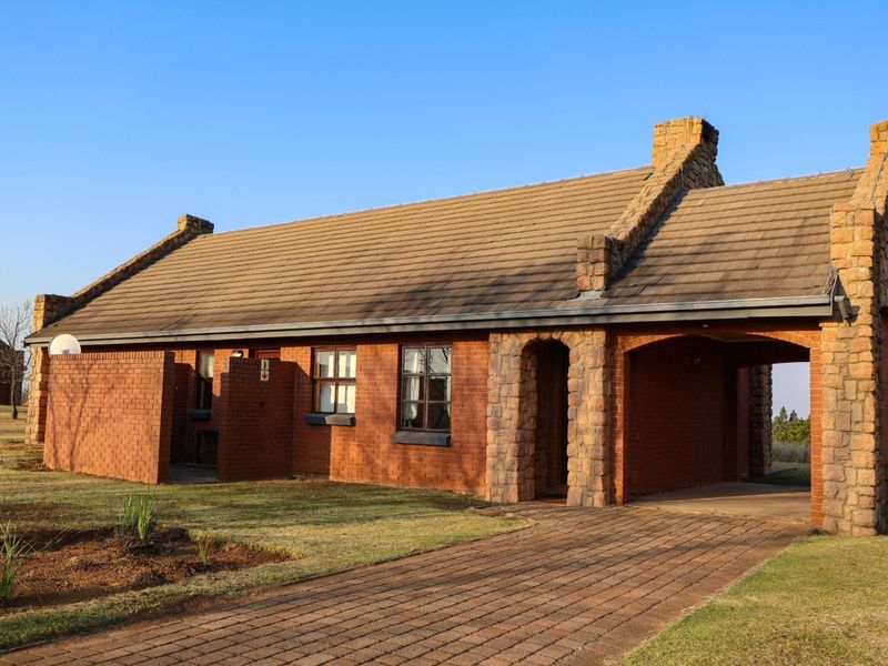 A charming face brick house featuring stone cladding accents, a tiled roof, and a paved driveway leading to a covered carport.