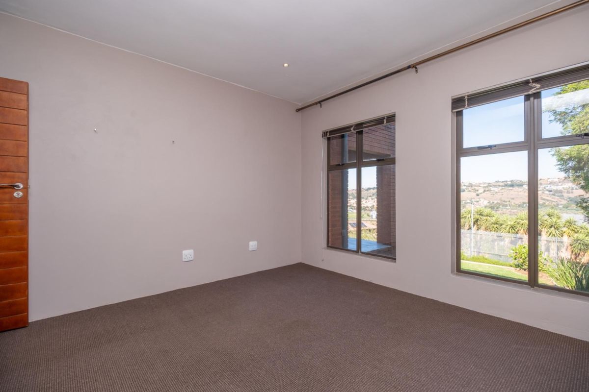 A bright, empty bedroom featuring neutral wall tones, carpeted flooring, and large windows that provide natural light and exterior views.
