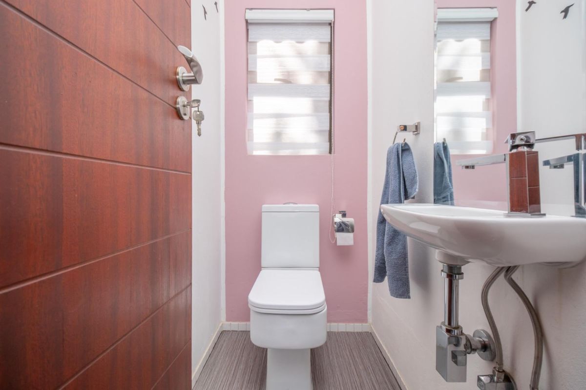 A compact guest bathroom featuring a modern white toilet, wall-mounted basin with chrome fixtures, and a window with a roller blind.