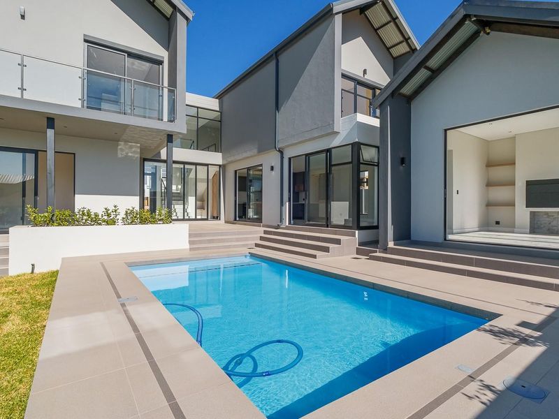 Modern architectural rear elevation featuring a swimming pool, tiled patio area, and seamless indoor-outdoor flow through large sliding glass doors.